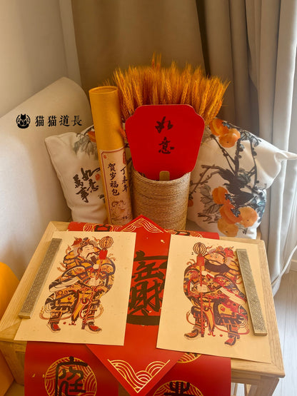 The door gods, the 招财进宝 square and the couplets laid out, with the 贺岁福包 gift tube behind them
